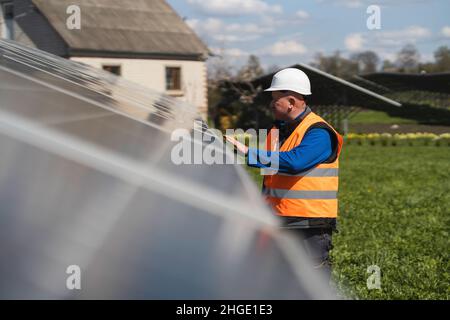 Ingegnere maschile in un elmetto e giubbotto riflettente ispeziona pannelli presso la centrale solare Foto Stock