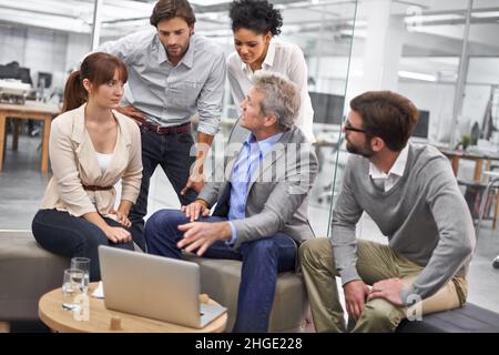 Radunato intorno ad un pro. Foto di un gruppo diversificato di professionisti dell'ufficio che parlano di un notebook. Foto Stock