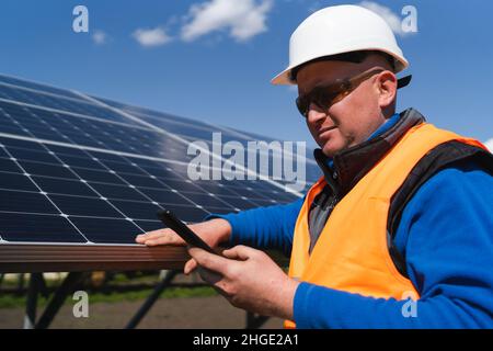 Uomo in elmetto utilizzando smartphone sullo sfondo dei pannelli solari Foto Stock