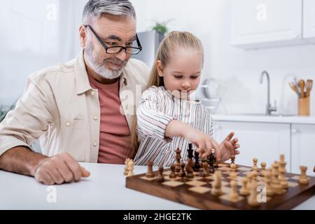 uomo anziano negli occhiali sorridendo vicino alla nipote che gioca a scacchi Foto Stock