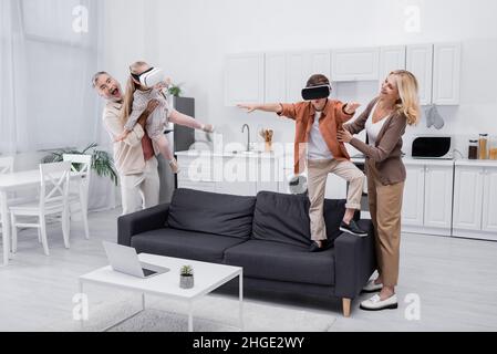 coppia entusiasta che si diverte con i nipoti con cuffie vr in cucina Foto Stock