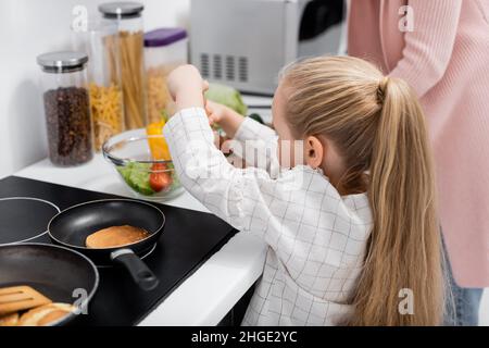 piccola ragazza che prepara insalata di verdure fresche con granato in cucina Foto Stock