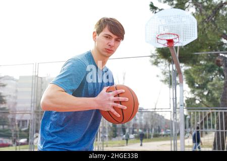 giovane atleta che si allena su un campo da basket all'aperto. uomo caucasico in abbigliamento sportivo che gioca a basket. Foto Stock