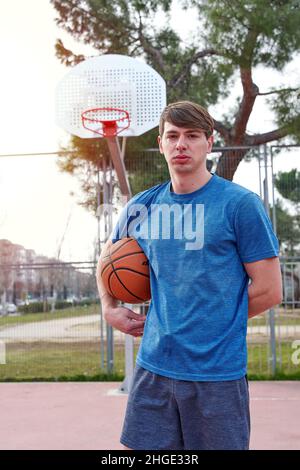 giovane atleta che si allena su un campo da basket all'aperto. uomo caucasico in abbigliamento sportivo che gioca a basket. Foto Stock