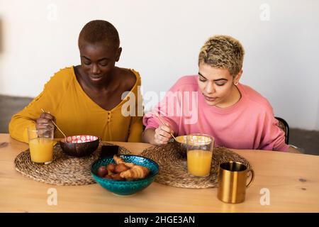 Felice coppia multietnica femmina rilassarsi a casa mentre si consuma la colazione Foto Stock