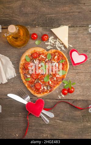 Pizza a forma di cuore con cuori su vecchio sfondo di legno, concetto di cena romantica per San Valentino. Foto Stock