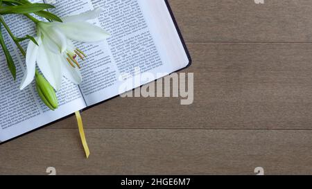 Giglio pasquale bianco adagiato su una bibbia aperta su un fondo di legno chiaro con spazio copia Foto Stock