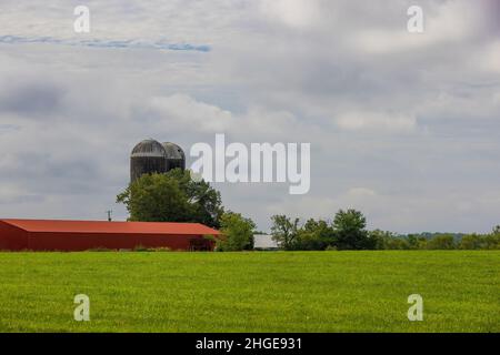 Rural Eastern Tennessee, paesaggio agricolo con silo sito su una collina accanto a un edificio rosso sotto cielo nuvoloso. Foto Stock
