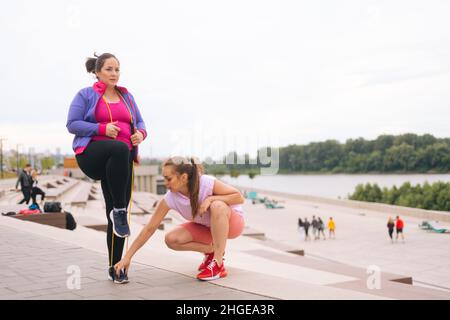 Motivato obese sovrappeso giovane donna facendo esercizi utilizzando nastro fitness per la perdita di peso con personal trainer all'aperto in estate giorno. Foto Stock