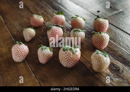 Piatto di frutta fresca. 3 file di pini su tavola di legno. Fragole bianche. Frutta di stagione Still Life. Berries rosa e bianco su sfondo scuro. Foto Stock