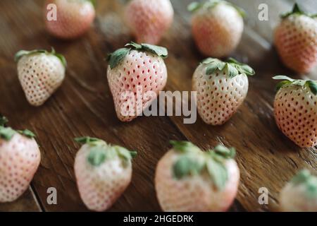 Piatto di frutta fresca. 3 file di pini su tavola di legno. Fragole bianche. Frutta di stagione Still Life. Berries rosa e bianco su sfondo scuro. Foto Stock