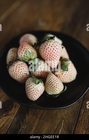 Piatto di frutta fresca. Pinacee su tavola di legno. Fragole bianche. Frutta di stagione Still Life. Berries rosa e bianco su sfondo scuro. Foto Stock