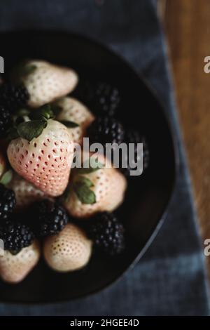 Fresh Fruit Flat posa in verticale. Pinacee e more su tavola di legno. Fragole bianche. Berries rosa e bianco. Foto Stock