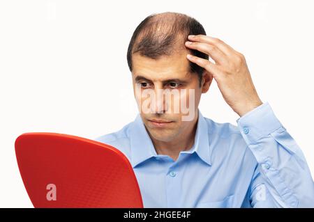 Sconvolto uomo di mezza età con alopecia guardando lo specchio, perdita di capelli concept Foto Stock