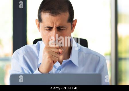 Scatto corto di un bel giovane uomo d'affari seduto da solo nel suo ufficio e tosse come soffre di un freddo Foto Stock
