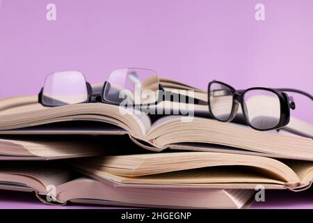 Libri aperti con bicchieri su sfondo rosa. Studio, istruzione e concetto di ritorno a scuola. Foto Stock