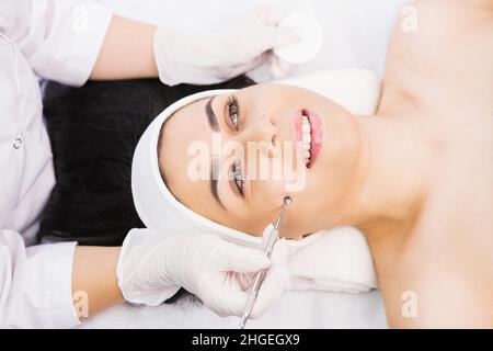 Il cosmetologo professionista esegue la procedura dermapen nella clinica di cosmetologia ad una donna, cosmetica del viso, pulizia manuale meccanica del viso con uno Foto Stock