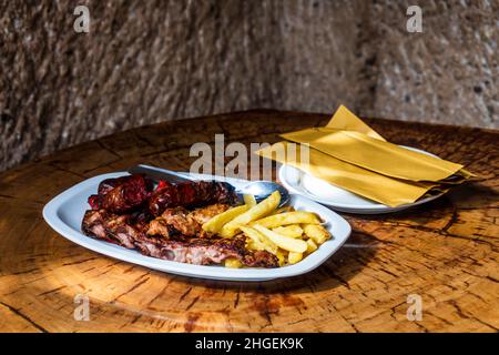 Carne mista alla griglia e servita con patatine fritte nel ristorante nella grotta, Guayadeque Ravine, Gran Canaria, Isole Canarie, Spagna Foto Stock