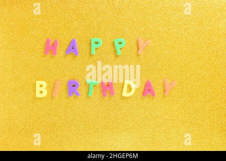 Fotografia di alcune lettere magnetiche con il testo inglese di Happy Birthday su sfondo dorato. La fotografia è scattata in formato orizzontale e da Foto Stock