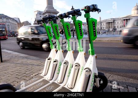 I veicoli passano una fila di scooter elettrici a noleggio parcheggiati nella baia dedicata, nel centro di Londra, Regno Unito Foto Stock