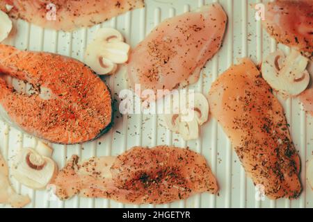 Foto di salmone. Pesce rosso fresco di colore ricco. Funghi e filetto di pollo alla griglia. Nelle spezie, basilico secco, sale, pepe. Salmone inon l'elettrico Foto Stock