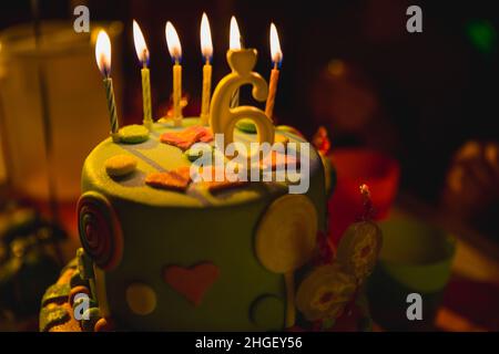 Torta di compleanno multicolore con candele a combustione e candela di 6 anni in fondo scuro con caramelle nel decor Foto Stock