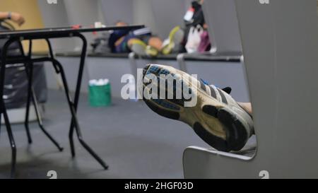 Boxer stanco mentre si siede sulla panca in spogliatoio. L'atleta stanco si trova nello spogliatoio. Un uomo molto stanco nella stanza degli spogliatoi, solo gamba visibile. Foto Stock