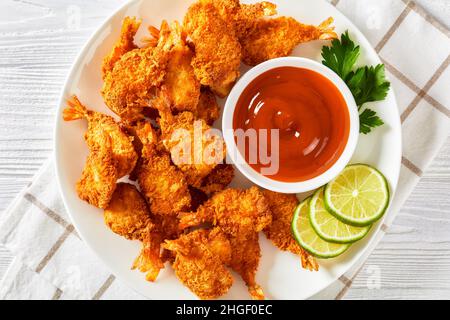Gamberi di farfalle fritti croccanti su un piatto bianco con salsa di zenzero mango e fettine di lime su un tavolo di legno bianco testurizzato, vista orizzontale da Foto Stock