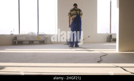 Lavori di ristrutturazione, levigatura parquet, lucidatura. L'uomo lucida i pavimenti in camera. Riparazione di appartamenti in una casa costosa. Foto Stock