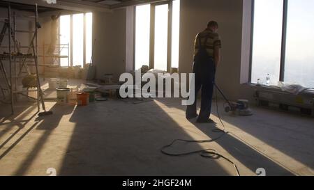 Lavori di ristrutturazione, levigatura parquet, lucidatura. L'uomo lucida i pavimenti in camera. Riparazione di appartamenti in una casa costosa. Foto Stock