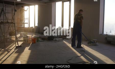 Lavori di ristrutturazione, levigatura parquet, lucidatura. L'uomo lucida i pavimenti in camera. Riparazione di appartamenti in una casa costosa. Foto Stock