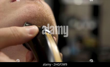Primo piano ritratto della vista laterale del giovane uomo bearded che ottiene la barba grooming nel barbiere moderno in slow motion. Parrucchiere al servizio del cliente, fare la barba Foto Stock
