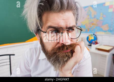 Insegnante premuroso in classe. Uomo con bearded pensivo con mano sul mento. Torna a scuola. Giornata degli insegnanti. Foto Stock