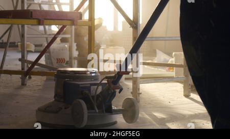 Lucidatrice per pavimenti. Lavori di ristrutturazione, levigatura parquet, lucidatura. L'uomo lucida i pavimenti in camera. Riparazione di appartamenti in un expe Foto Stock