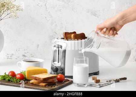 Donna che versa il latte in un bicchiere vicino al tostapane in cucina Foto Stock