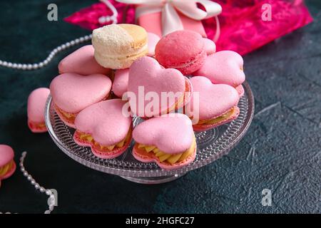 Dessert stand con gustosi macaroni a forma di cuore su sfondo nero Foto Stock