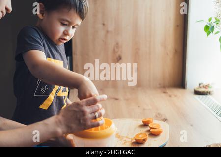 Mamma che aiuta suo figlio a spremere l'arancia fresca per fare succo. Cibo vegetariano. Cibo dolce. Succo di frutta. Cibo sano. Foto Stock