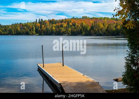 Coloratissimo fogliame autunnale sul lago Caribou nel Minnesota settentrionale, con un molo per barche, boschi e increspature bellissime sull'acqua blu su un motto parzialmente soleggiato Foto Stock