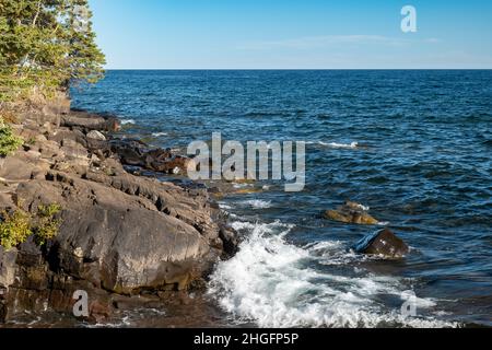 L'onda bianca che si avvolse dall'acqua blu del lago Superior si spruzza sulla costa nord rocciosa del Minnesota. Questo grande lago è chiamato Gitchi-Gami da Foto Stock