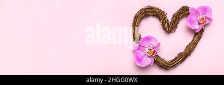 Corona di rattan a forma di cuore decorata con fiori tropicali di orchidea su sfondo rosa Vista dall'alto Flat Lay Holiday card buon San Valentino, amore con Foto Stock