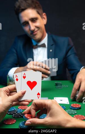 Vista ravvicinata delle mani delle donne con carte da gioco e fiches al tavolo verde del casinò con il giocatore di poker. Foto Stock