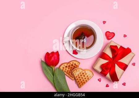 San Valentino prima colazione a letto. Regalo, tè belga cialde fiore, , cuori su sfondo rosa. Concetto di giorno di San Valentino. Foto Stock