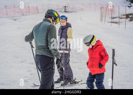 Mamma e figlio imparano a sciare con un istruttore. Bambino attivo con casco, occhiali e pali di sicurezza. Gara di sci per bambini piccoli. Inverno Foto Stock