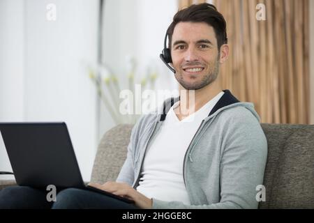 uomo in cuffia che lavora con il laptop da casa Foto Stock