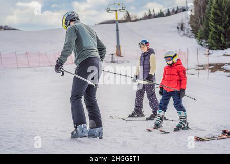 Mamma e figlio imparano a sciare con un istruttore. Bambino attivo con casco, occhiali e pali di sicurezza. Gara di sci per bambini piccoli. Inverno Foto Stock