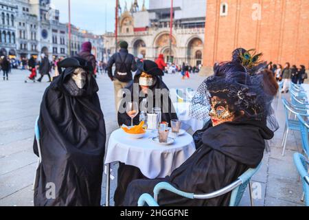 Gruppo di persone in abito elegante costume storico e maschera si siedono per un drink in un caffè in Piazza San Marco, Carnevale di Venezia, Carnevale di Carnevale die Venezia, Italia Foto Stock