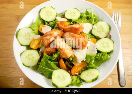 Insalata fresca con cubetti di salmone teriyaki alla griglia, pezzi di formaggio sul letto di lattuga primaverile con cetriolo e pomodori Foto Stock