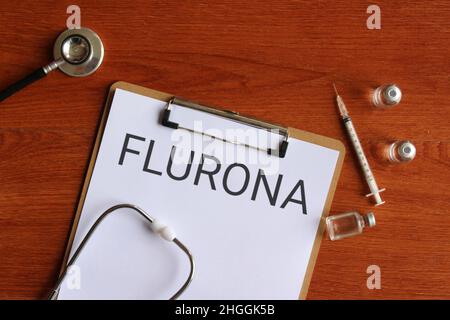 Concetto medico e sanitario. Immagine vista dall'alto di stetoscopio, siringa, flaconcino di vetro e appunti di carta con testo FLURONA. Foto Stock