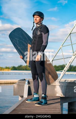 Ritratto a tutta lunghezza del wakeboarder con bordo in piedi sul molo Foto Stock