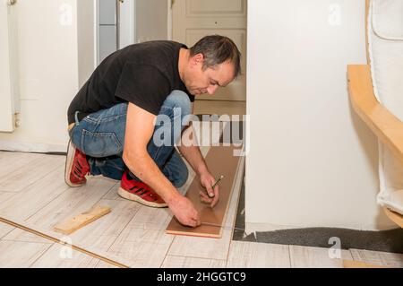 Uomo che lavora con le dita amputate. Sta lavorando alla posa del pavimento in casa sua durante il giorno. Foto Stock